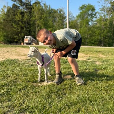 A boy with a miniature goat on a leash outdoors.