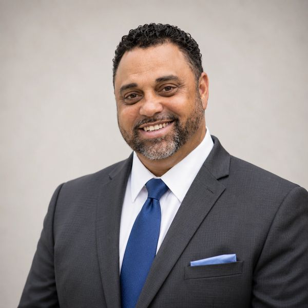 Smiling man in a dark suit and blue tie.