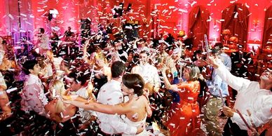 People dancing in a room with red uplights and confetti flurrying all around them.
