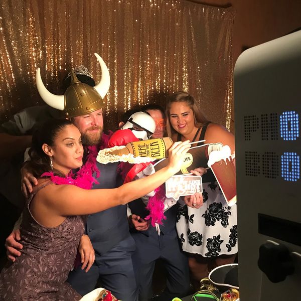 A group of 4 guests taking a picture with the photobooth while holding props with a gold backdrop.