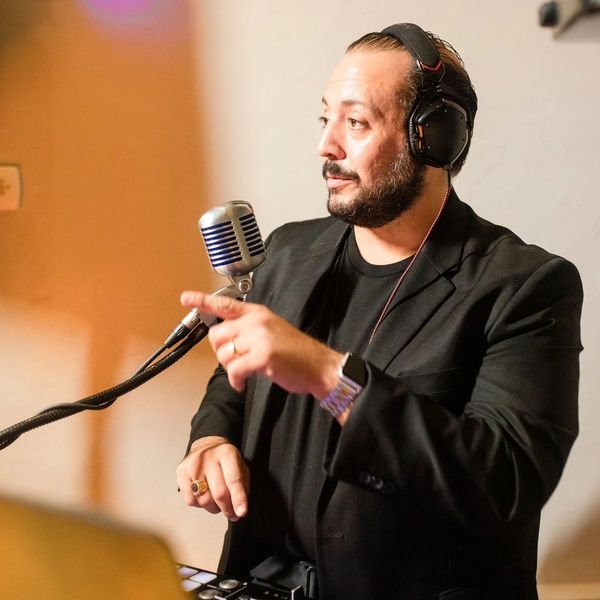 Picture of DJ Stephen Peters wearing a black suit with his headphones and a microphone
