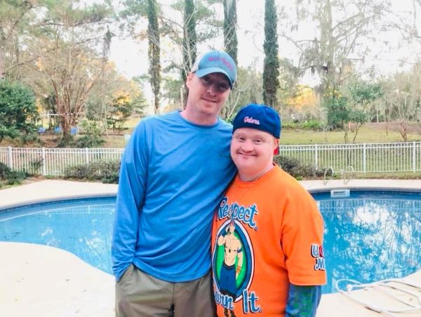 Two men smiling by a backyard pool on a sunny day.