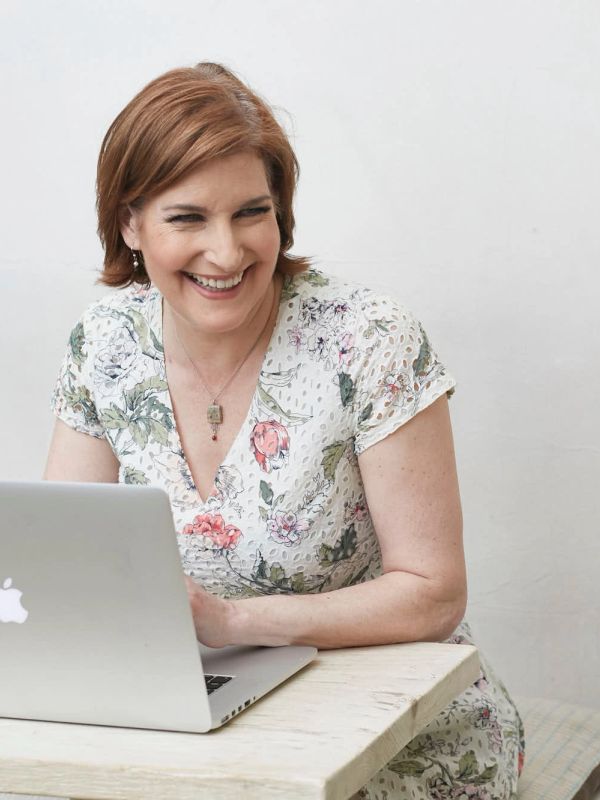 Woman in floral dress smiling at laptop.