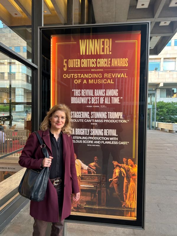 Woman standing near a theater sign for an award-winning musical revival.