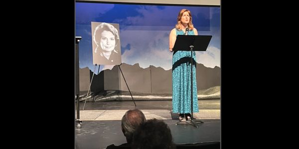 A woman speaking at a podium beside a black-and-white photo on an easel.