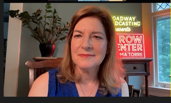 Woman sitting indoors with neon signs and plants behind her.