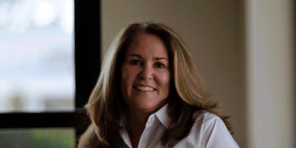 Smiling woman in a white shirt indoors near a window.