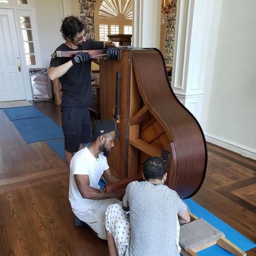 The crew putting legs back on a baby grand piano and preparing to set it up in the customer's home