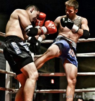 Two Muay Thai fighters in a ring during a match, one delivering a kick.