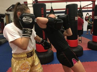 Two women sparring in a boxing gym with gloves and shorts.