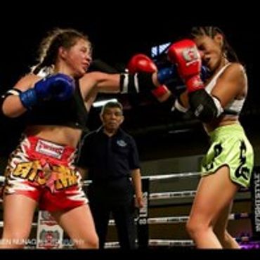 Two female Muay Thai fighters in action in a boxing ring with a referee.