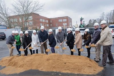 Group of people in hard hats performing a groundbreaking ceremony with shovels.