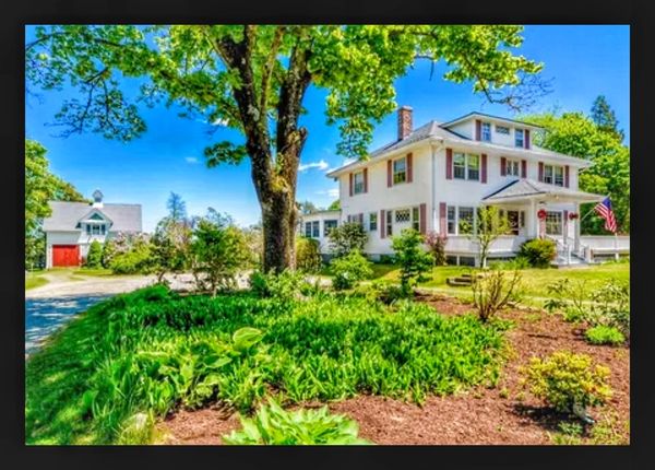 Large white house with green yard and bright blue sky.