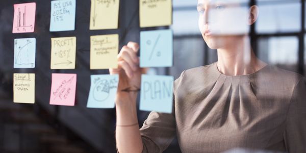 Businesswoman planning strategy using sticky notes on glass.