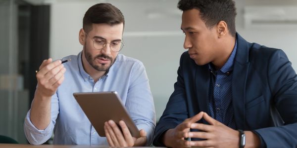 Two businessmen discussing information on a tablet in a meeting room.