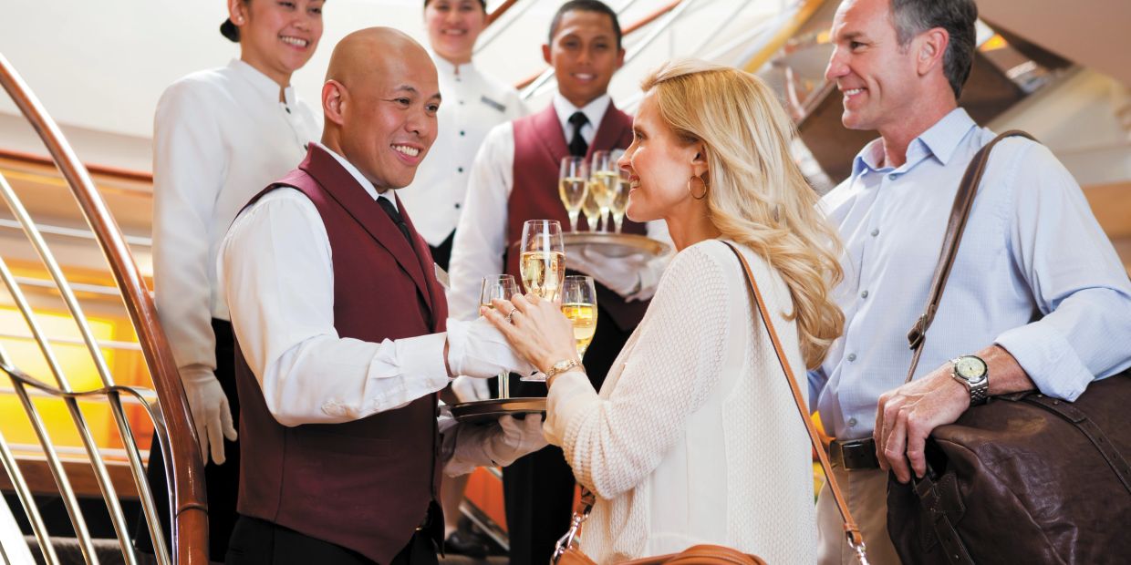 Couple receiving champagne from smiling waitstaff.