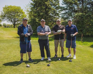 Four men standing on a golf course holding golf clubs.