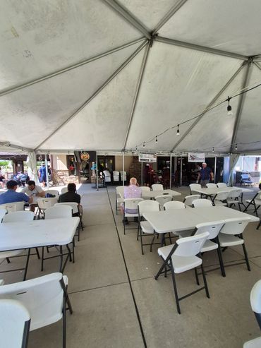 Outdoor tent with white tables and chairs, a few people seated.