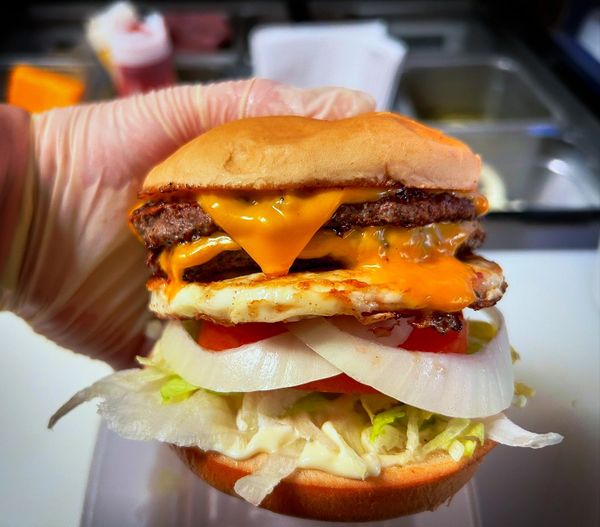 Double cheeseburger with Egg all the way being held in hand