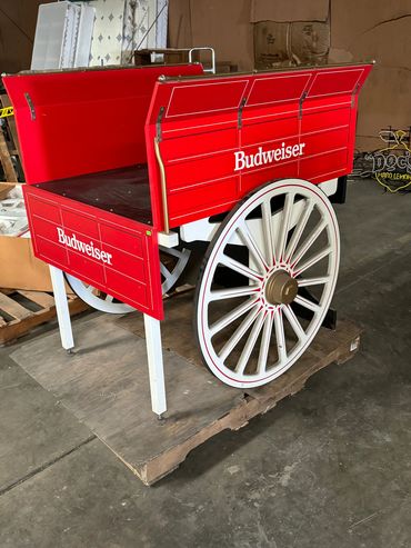 A red Budweiser wagon with large white wheels on a wooden pallet.