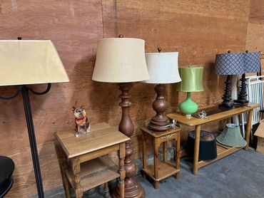 A collection of various lamps and small wooden tables against a wooden wall.