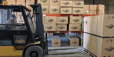 A forklift lifts boxes labeled VELOC in a warehouse.