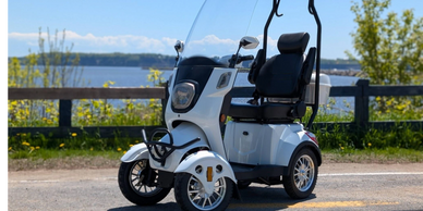 White electric mobility scooter parked near a waterfront on a sunny day.