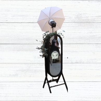 A standing mirror with a light umbrella and a woman in a black dress reflected.