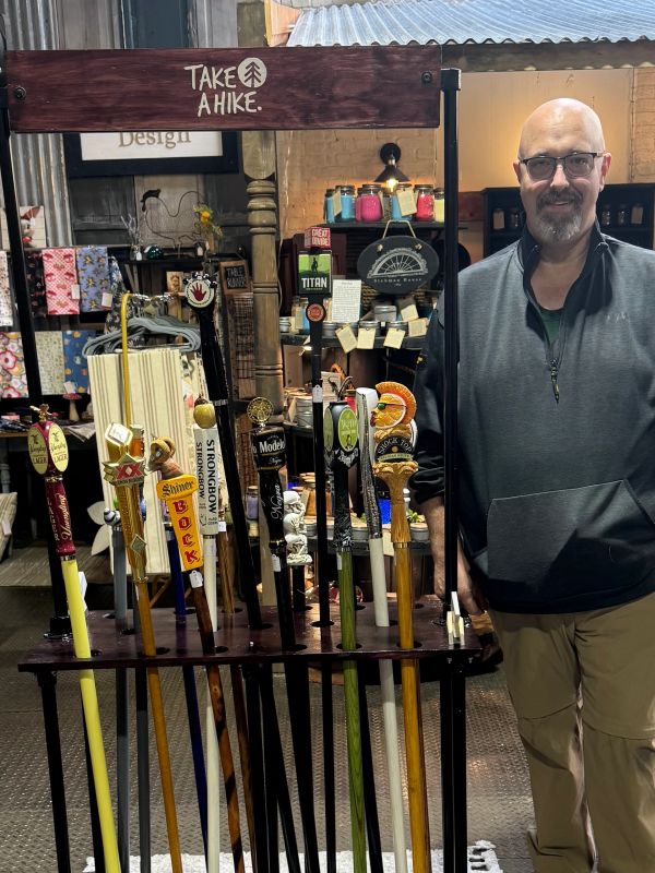 Man standing next to a display of decorative hiking sticks with beer tap handles.