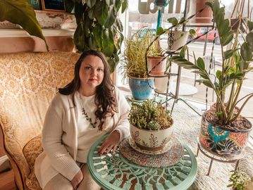 Woman sitting next to potted plants on a patterned table.