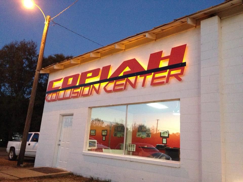 Exterior of a collision center with illuminated signage at dusk.