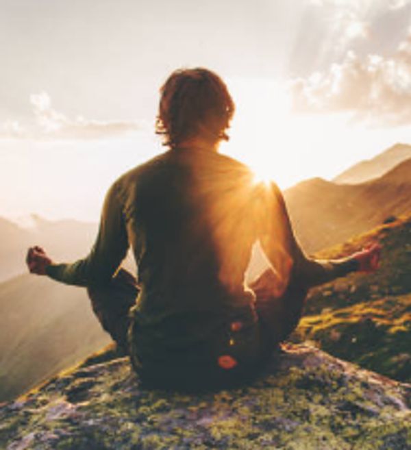 Person meditating on mountain at sunset.