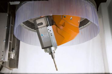Close-up of an orange robotic arm with a drill bit inside a machine.