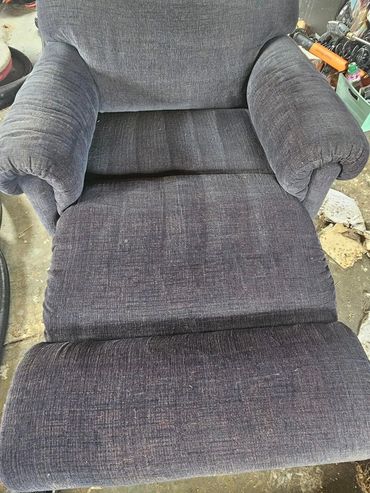 A worn gray recliner chair in a cluttered space.