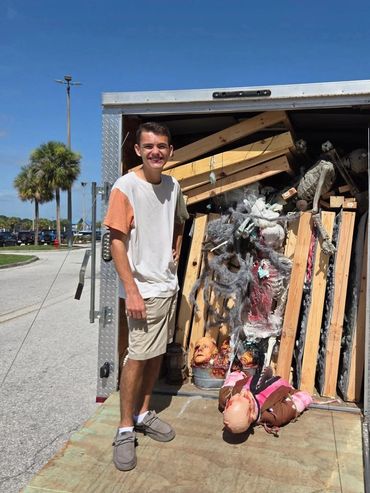 Young man standing next to a trailer filled with Halloween decorations.