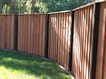 Curved wooden fence with vertical planks and black posts in a sunny backyard.