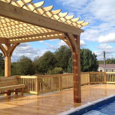 Wooden pergola on a deck beside a swimming pool under a partly cloudy sky.