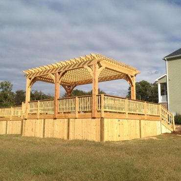 A wooden pergola on an elevated deck with a fenced yard.