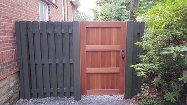 A wooden garden gate with black fence panels on a gravel path.