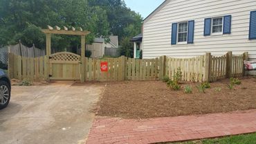 New wooden fence with a gate and arch in front of a house.