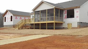Newly constructed house with a wooden deck and adjacent building under construction.