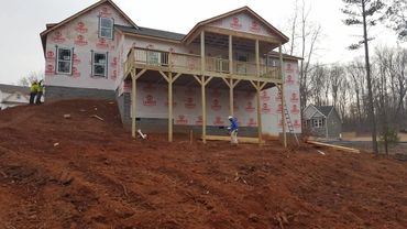 House under construction with a wooden balcony on a dirt hill.