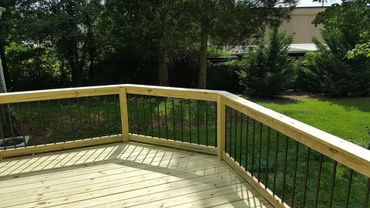 New wooden deck with black metal railings overlooking a green backyard.