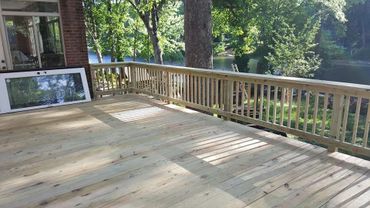 New wooden deck overlooking a peaceful lake surrounded by trees.