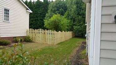 A wooden fence separating two houses with green grass and trees.