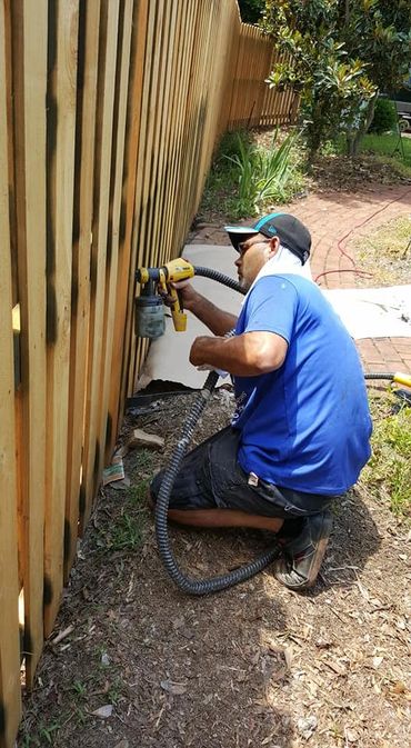Man spray painting a wooden fence outdoors on a sunny day.