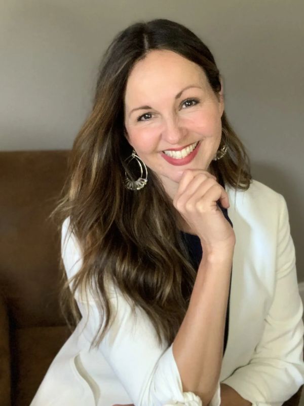 Smiling woman with long brown hair wearing a white blazer.