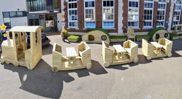Wooden playground train with picnic tables in carriages and crawl tunnel to front.