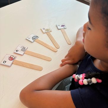 Child arranging popsicle sticks with animal pictures and letters on a table.