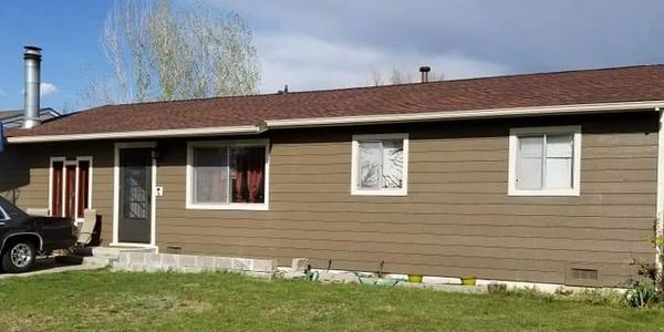 Single-story brown house with a large grassy front yard under a partly cloudy sky.